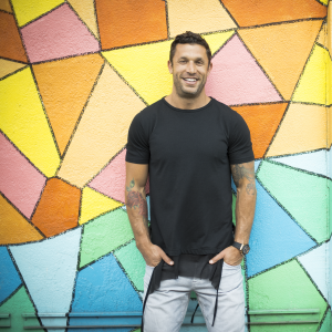 Aubrey Marcus in front of a wall that has been painted with geometric shapes in rainbow colors.