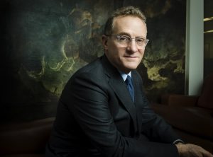 Howard Marks in front of a dramatic painting of a storm at sea.