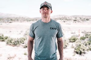 Nick Norris in a CKIV t-shirt and camo ball cap, standing outside in desolate wilderness.