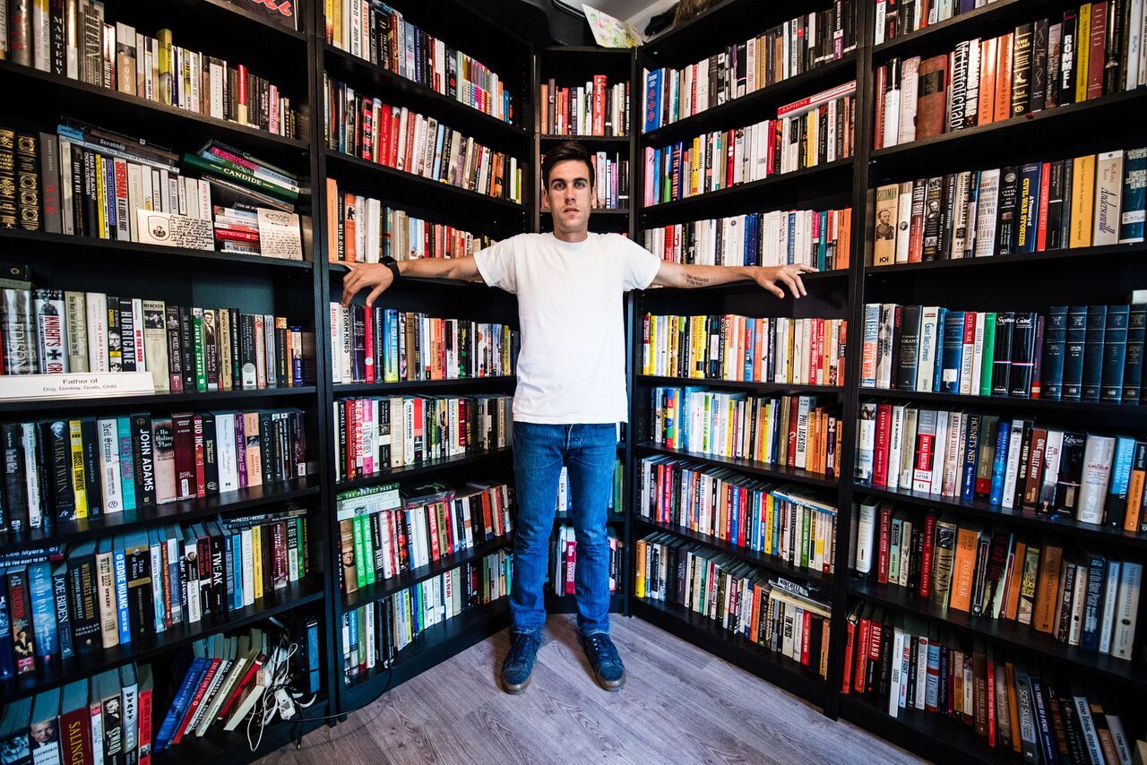 Ryan Holiday standing in front of his very full bookshelves.