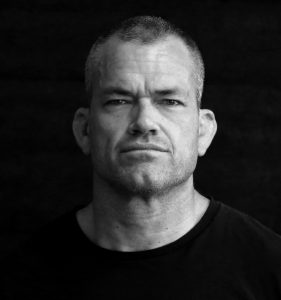 Jocko Willink in a dark t-shirt and black background.