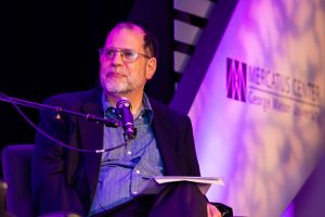Tyler Cowen sitting onstage at a microphone.