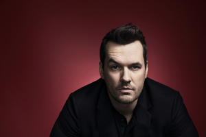 Jim Jefferies in a black shirt and raising an eyebrow.