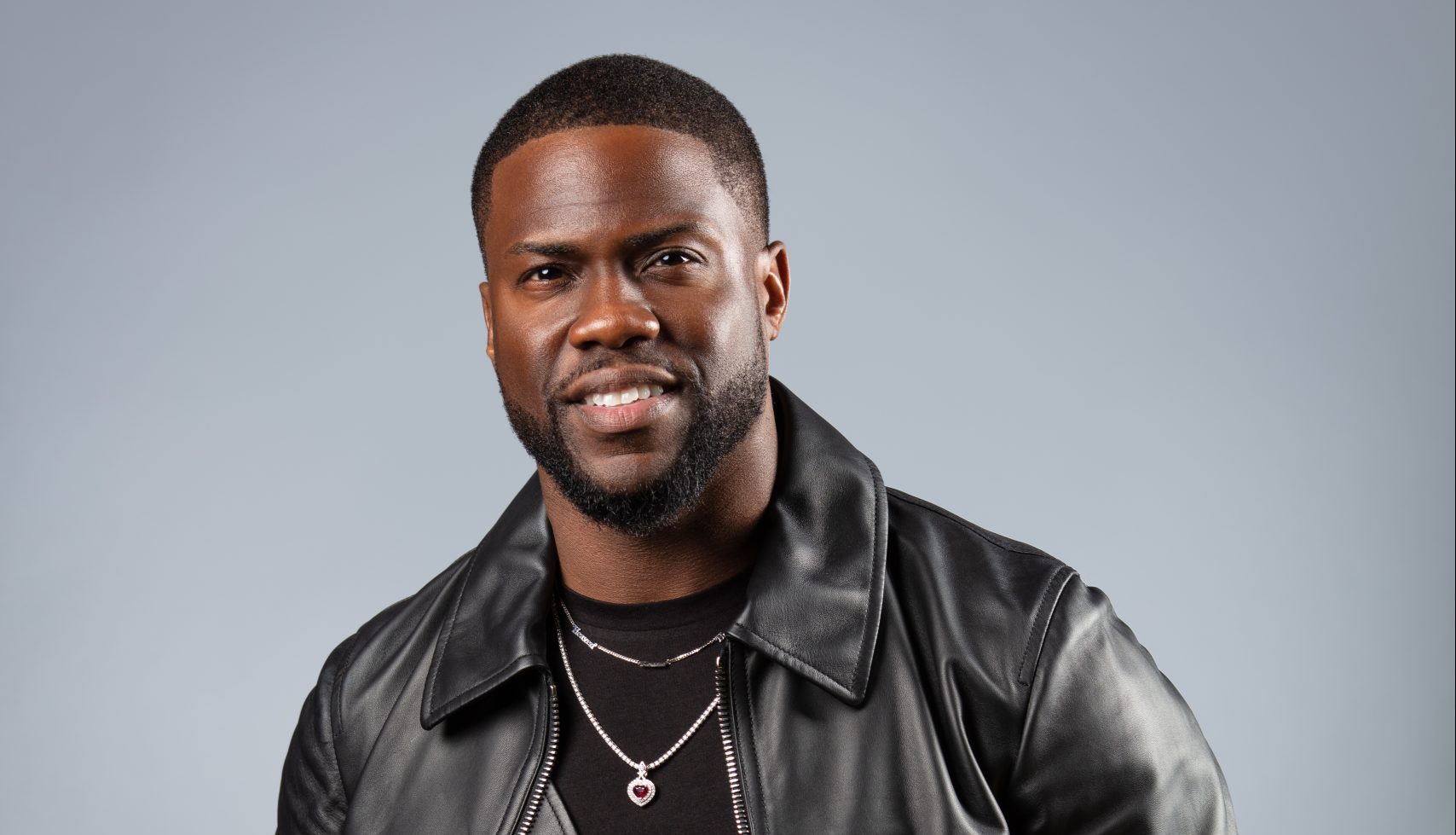 Kevin Hart in a black leather jacket, smiling.