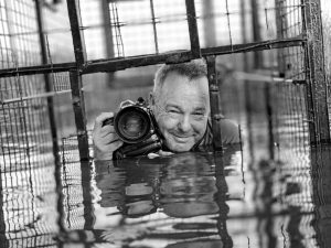 David Yarrow half-submerged in a shark cage in water.