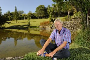 Richard Koch sitting crosslegged by a lake.