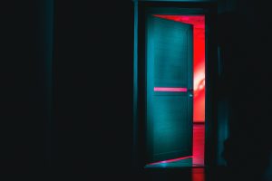 A door in a dark room opening onto another room bathed in red light.
