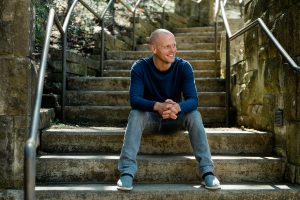 Tim Ferriss sitting outdoors on some stone steps and smiling.